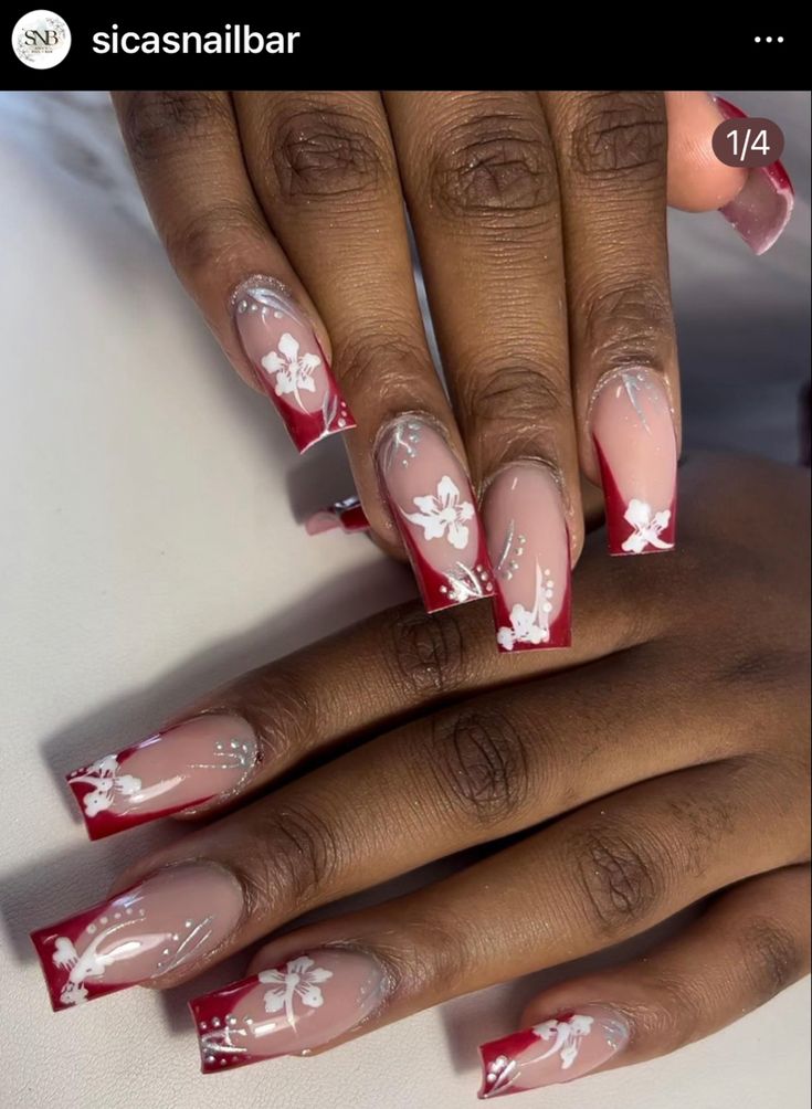 Sophisticated Nail Design: Soft Nude Base with Bold Red Tips and Delicate White Floral Patterns.