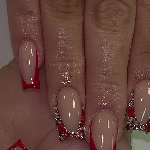 Chic Nude Nails with Striking Red Tips and Shimmering Rhinestone Accents.