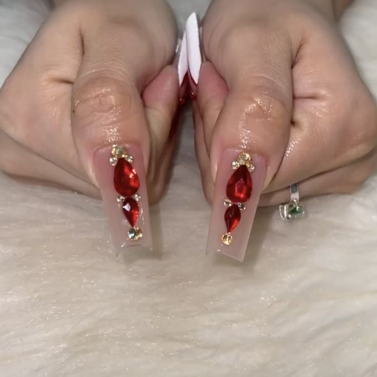 Sophisticated Red Gemstone Nail Design with Elongated Clear Tips and Teardrop Accents.