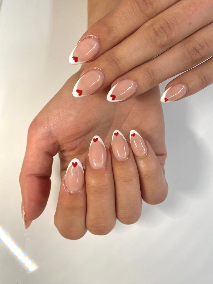 Charming French Manicure with Nude Base, White Tips, and Delicate Red Heart Accents.