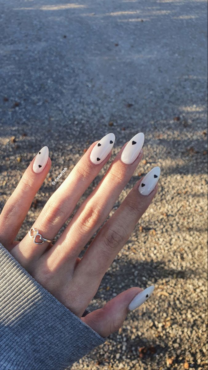 Trendy Almond-Shaped Nails with Soft White Polish and Playful Black Heart Accents.