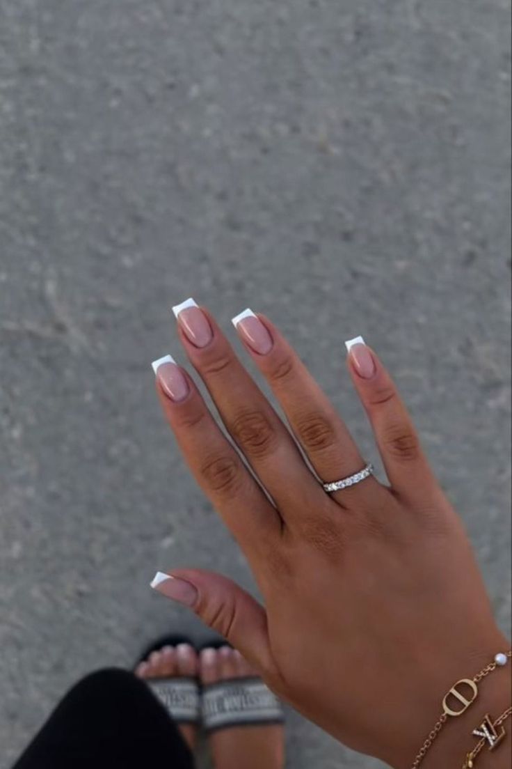 Chic French Tip Manicure with Nude Base and Sparkling Jewelry Accents.